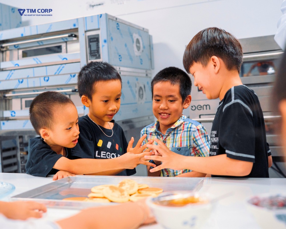 Các bé trai vui vẻ cùng nhau làm bánh trong không gian trải nghiệm F&B tại lớp học thực hành.