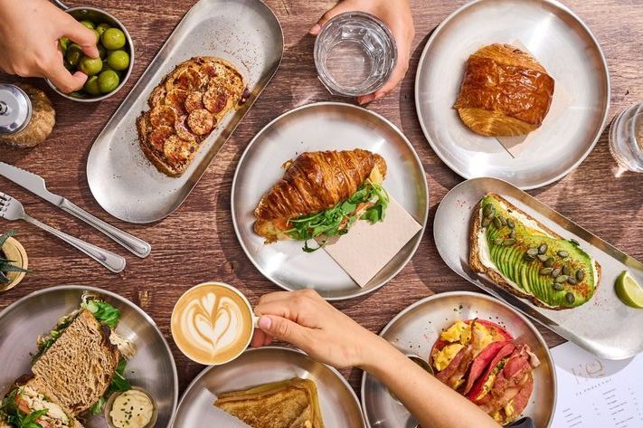 Thành phẩm đa dạng từ nghề làm bánh: bánh croissant, sandwich, cà phê latte và bánh mì trang trí tinh tế trên bàn ăn.