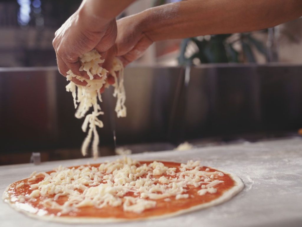 Đôi tay rắc phô mai lên pizza – minh chứng cho sự sáng tạo và nghệ thuật trong nghề làm bánh hiện đại.