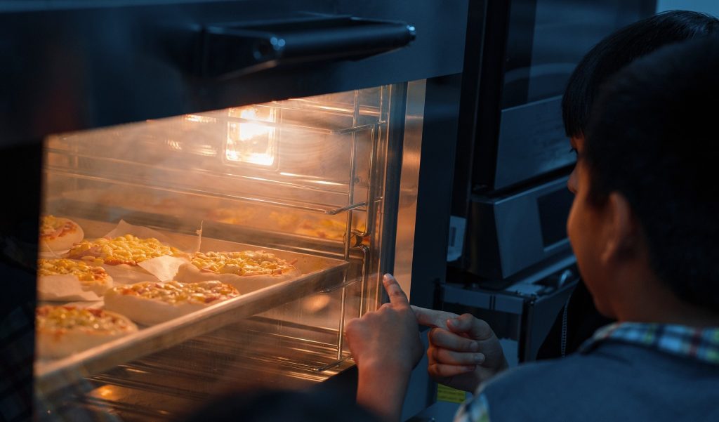 Khoảnh khắc quan sát pizza chín vàng trong lò nướng hiện đại tại lớp học trải nghiệm làm pizza.