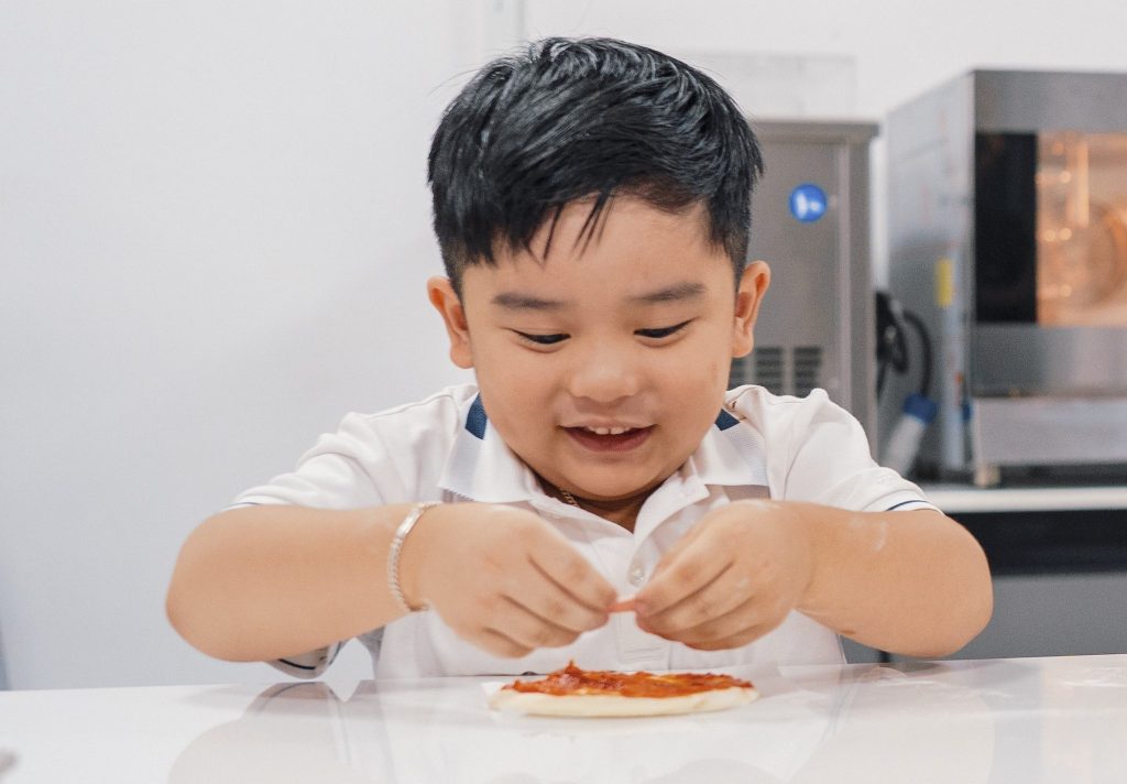 Bé trai tập trung thực hiện thao tác ẩm thực, tự tay hoàn thiện món ăn và khám phá ẩm thực theo cách của riêng mình.